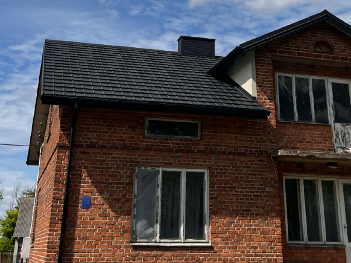 Dom z czerwonej cegły z nowym ciemnym dachem po remoncie